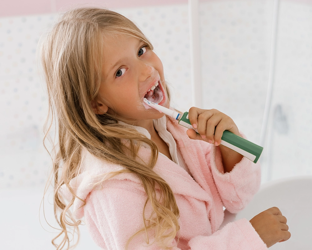 Niña lavándose los dientes con cepillo eléctrico.