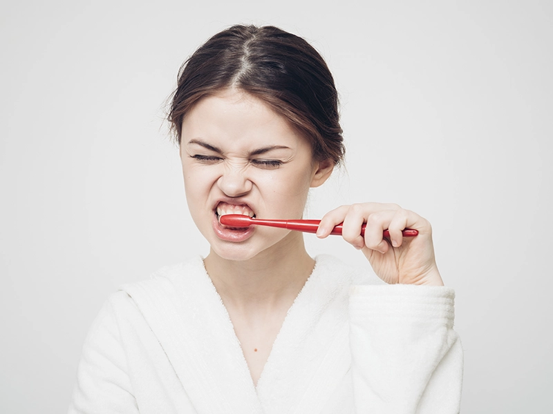 Una chica cepillándose los dientes muy fuerte.