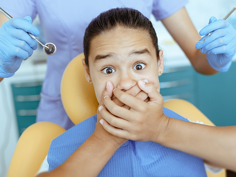 Una niña tapándose la boca cuando está en el sillón del dentista.